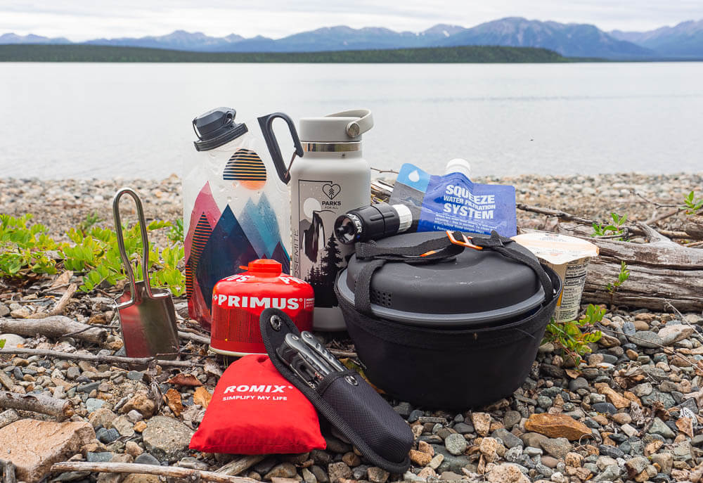Different camping cooking utensils in front the beautiful Lake Clark and mountains