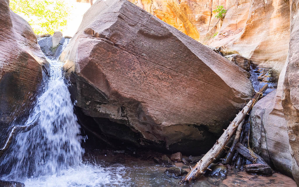 Waterfall coming down next to a boulder. You can climb up a log