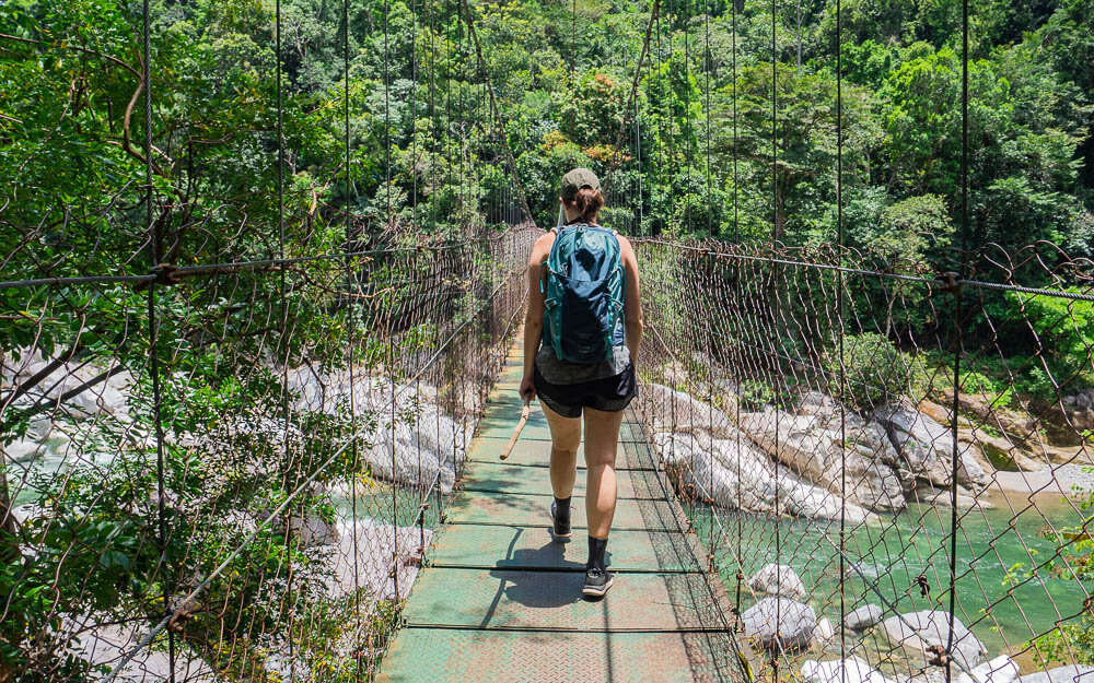 Dana walking over a suspension bridge wearing summer hiking clothes