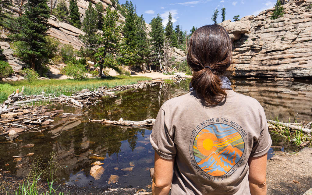 Dana standing in front of a lake wearing her Rocky Mountains National Park t-shirt